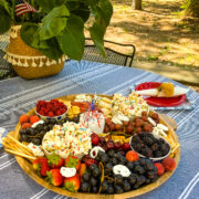 Red, white and blue charcuterie board on blue tablecloth with plant in background.