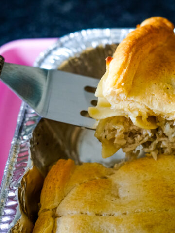 Metal spatula lifting up chicken casserole topped with pillsbury crescent rolls.
