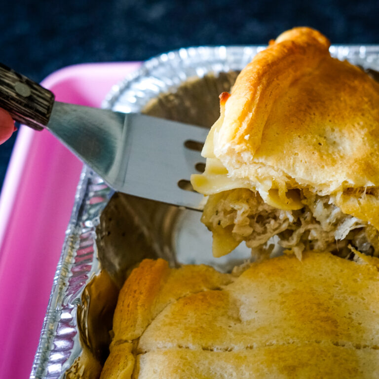Metal spatula lifting up chicken casserole topped with pillsbury crescent rolls.