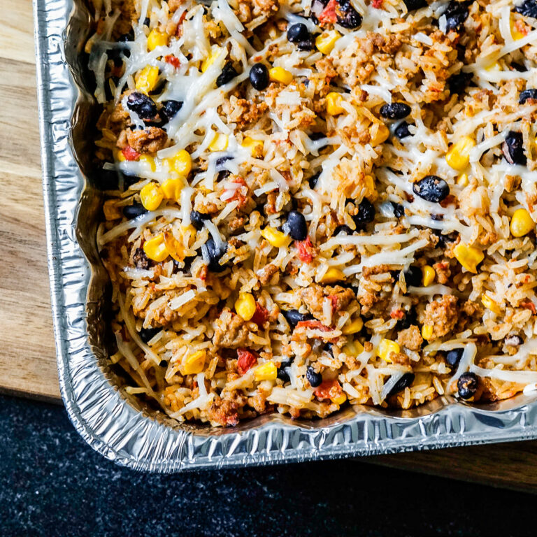 Metal pan filled with baked casserole with rice, black beans, corn, tomatoes and shredded mozzarella cheese.