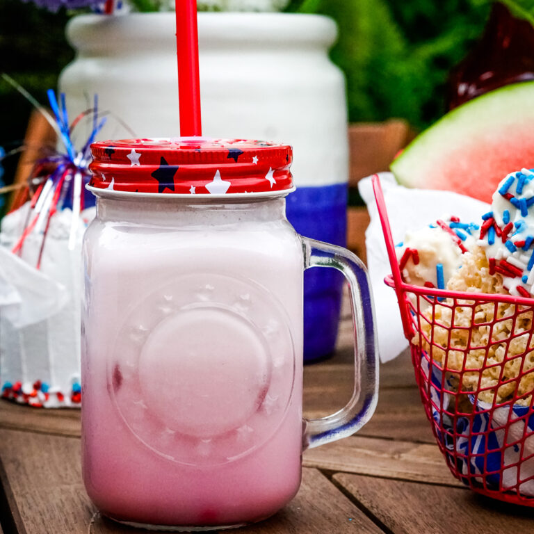 Frosted lemonade in a glass jar with a handle and a red white and blue lid with a straw.