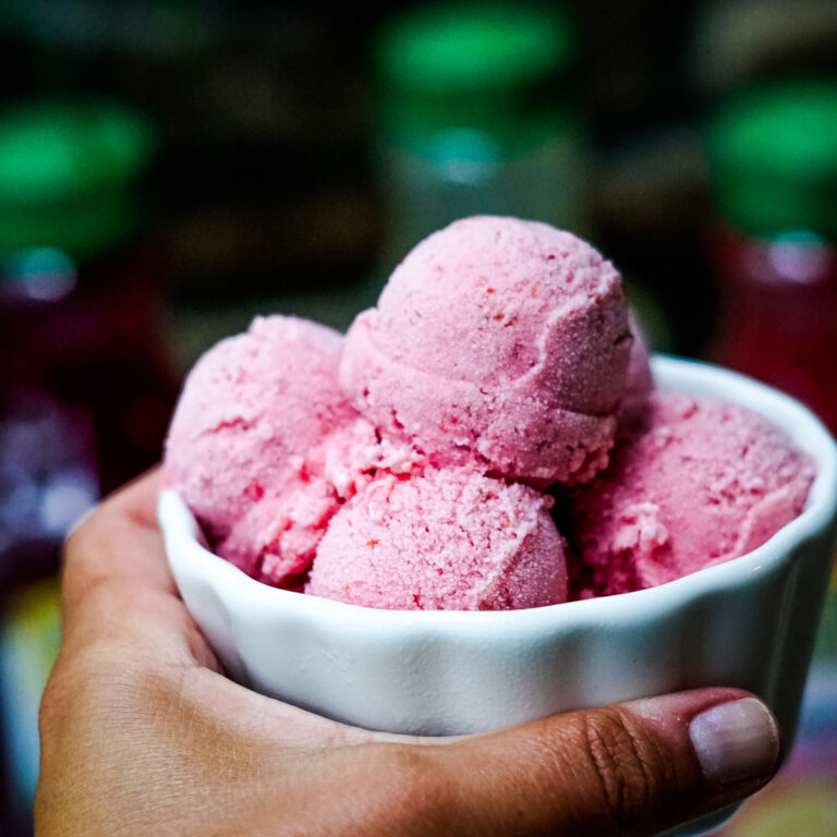 Hand holding a small bowl of purple blackberry frozen whip.