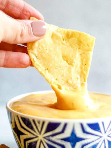 Hand holding corn tortilla tip and dipping it into Copycat Taco Bell Nacho Cheese Sauce in blue bowl.