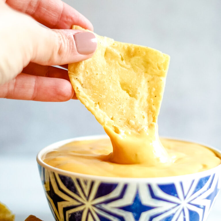 Hand holding corn tortilla tip and dipping it into Copycat Taco Bell Nacho Cheese Sauce in blue bowl.