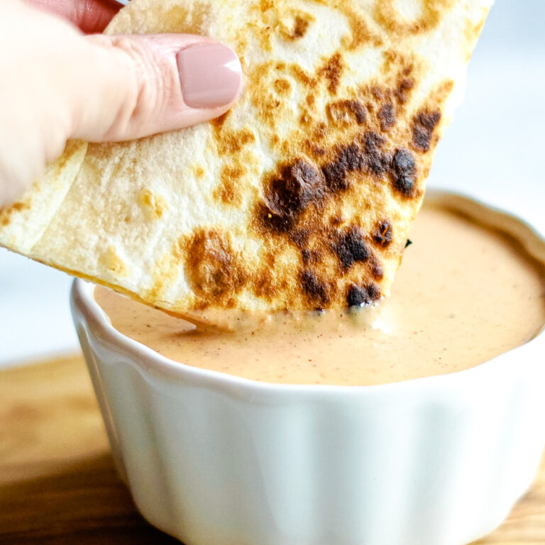 Grilled flour quesadilla triangle being dipped into taco bell copycat quesadilla sauce.