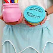 Woman holding markers in one hand and food storage container with silicone lid in the other hand. She's wearing a blue apron. Lid has a joke written on it in sharpie.