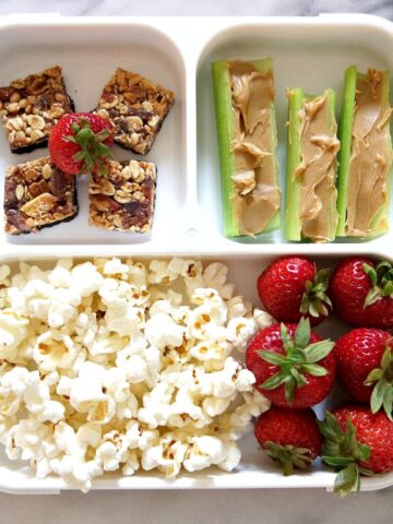 Popcorn, strawberries, celeries with peanut butter and granola squares in Bento lunch box