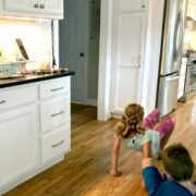 Two kids doing a crab walk in a kitchen, while playing Animal Workout on an Alexa Device