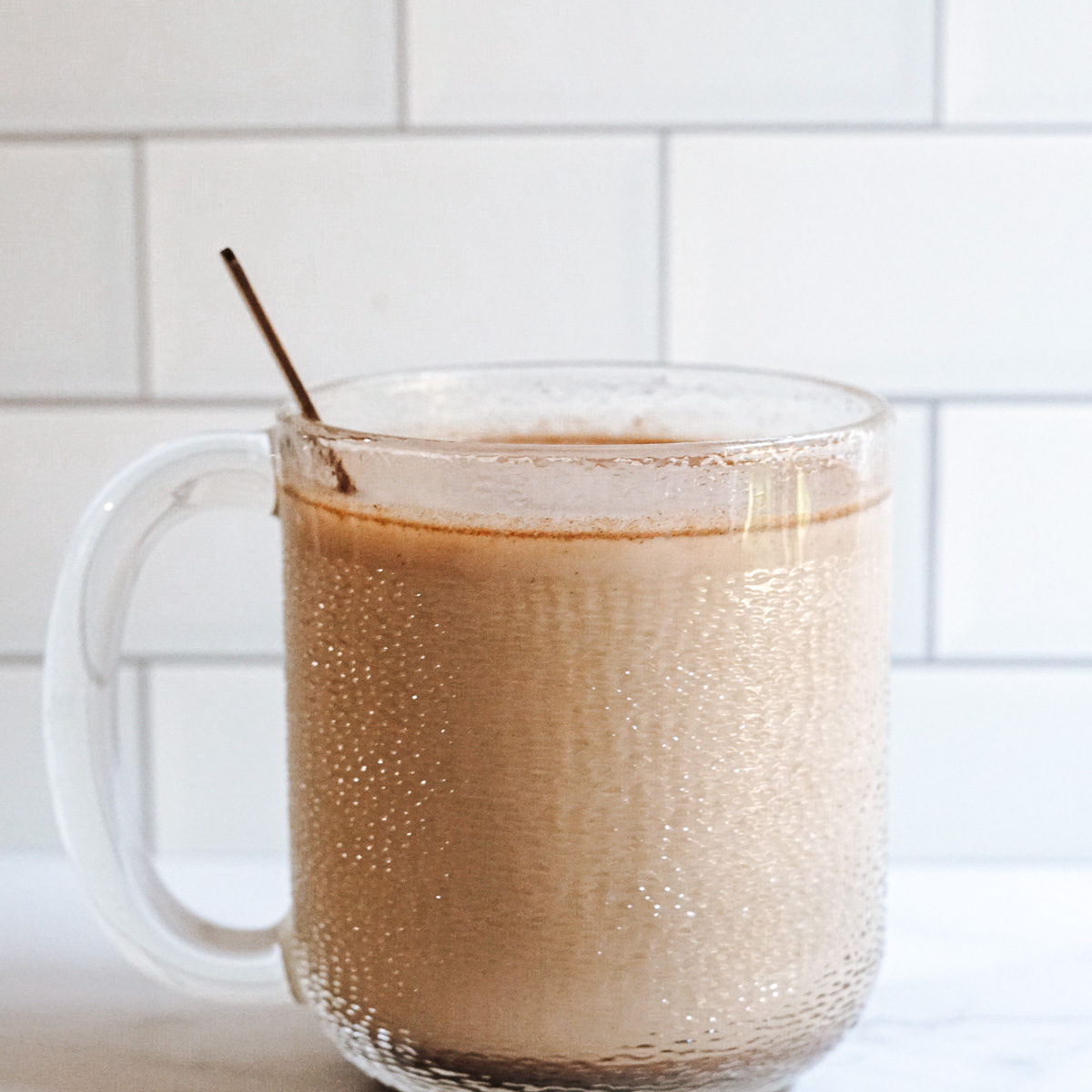 Creamy tan colored coffee drink in clear mug with spoon sticking out of it. Contains coffee, milk and ashwagandha.