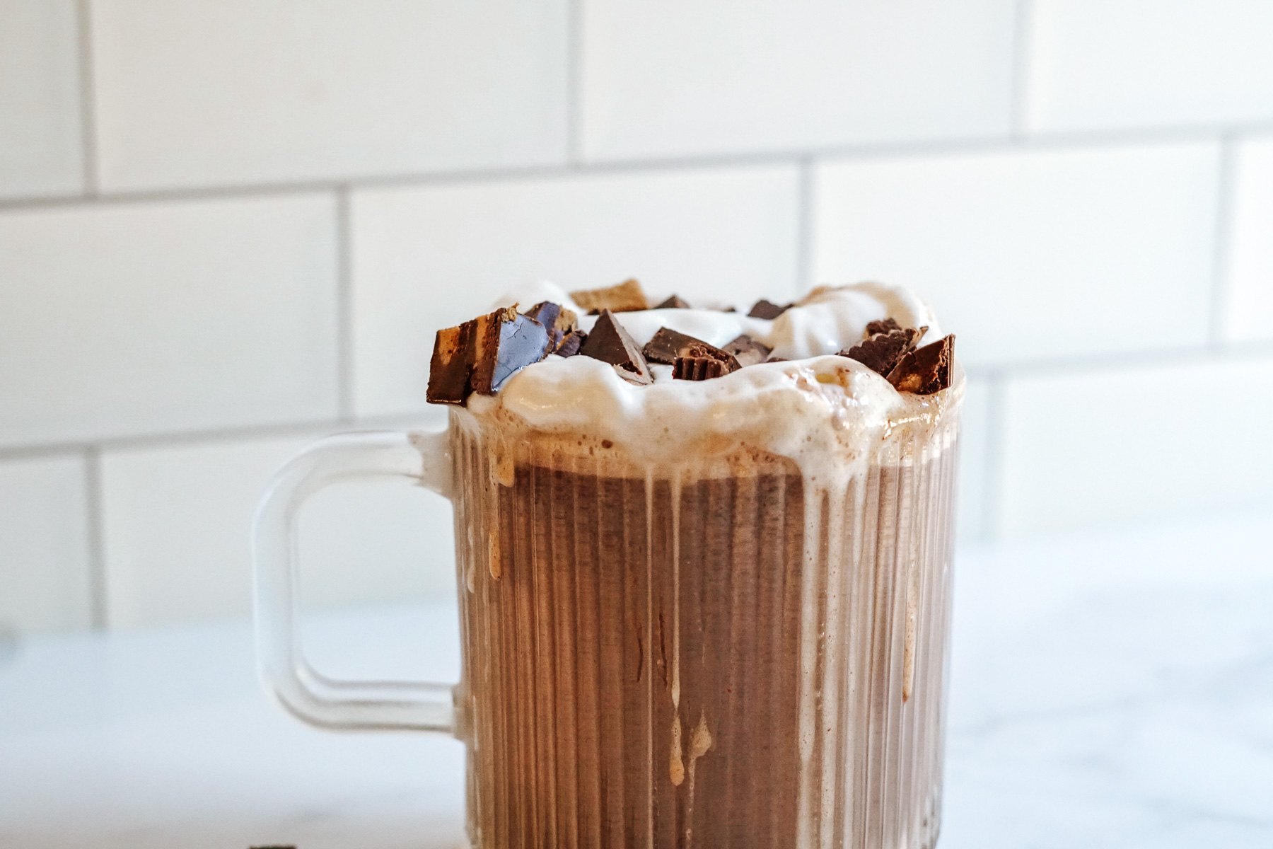 Hot chocolate in clear mug topped with whipped cream and chopped Reese's Peanut Butter Cups.