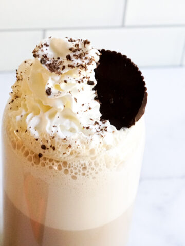 Bailey's Irish Cream and Peanut Butter Cup Latte in a clear glass topped with whipped cream, chocolate shavings and a peanut butter cup.