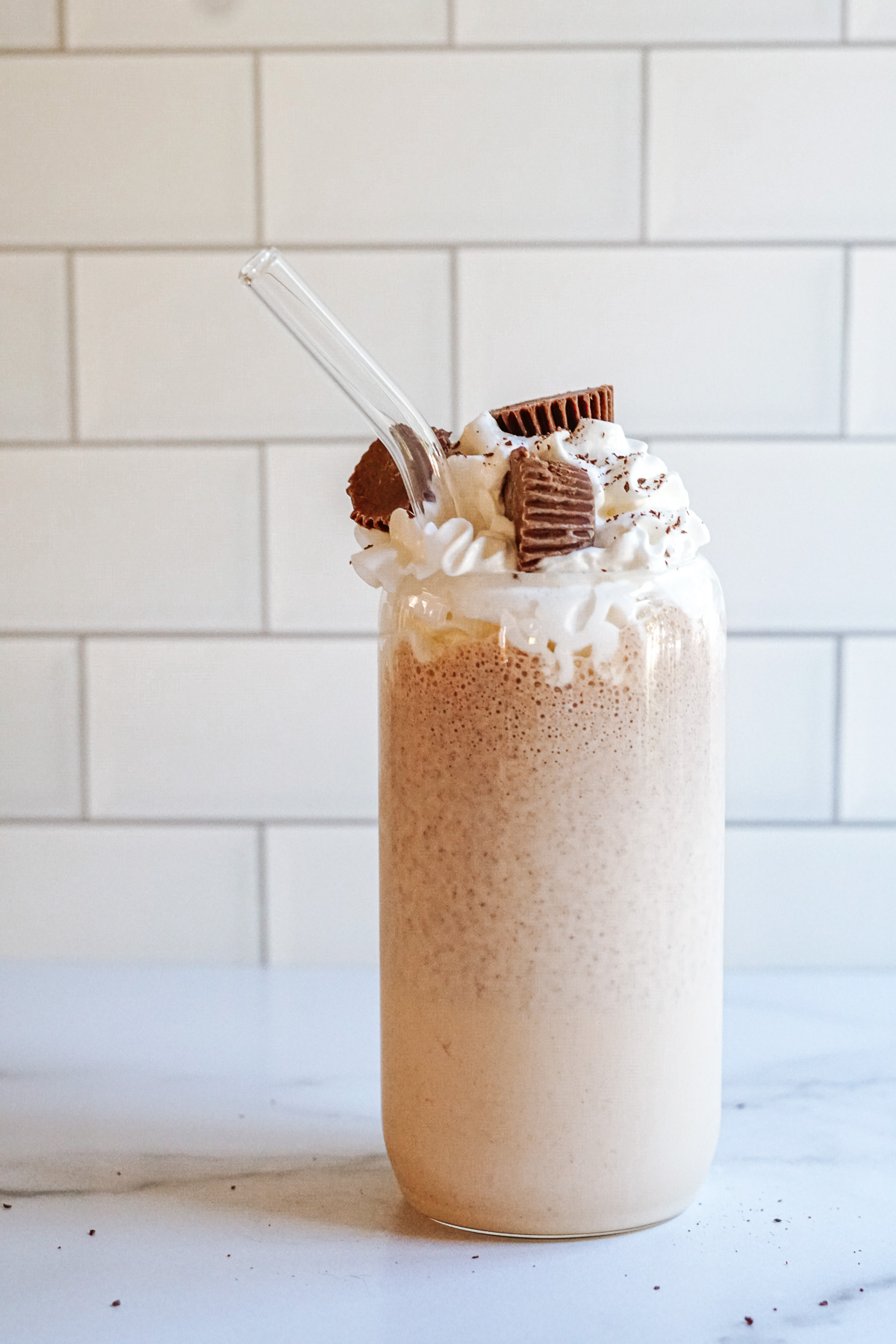 Bailey's Irish Cream and Peanut Butter Cup Milkshake in a clear glass topped with whipped cream, chocolate shavings and peanut butter cups.