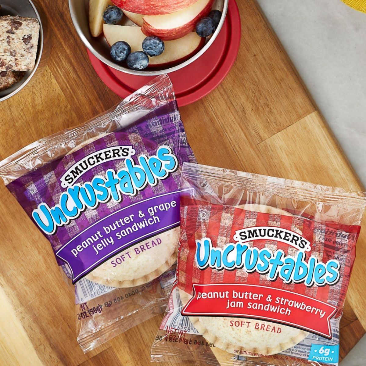 Two uncrustables sandwiches inside their plastic bags on top of a wooden cutting board.