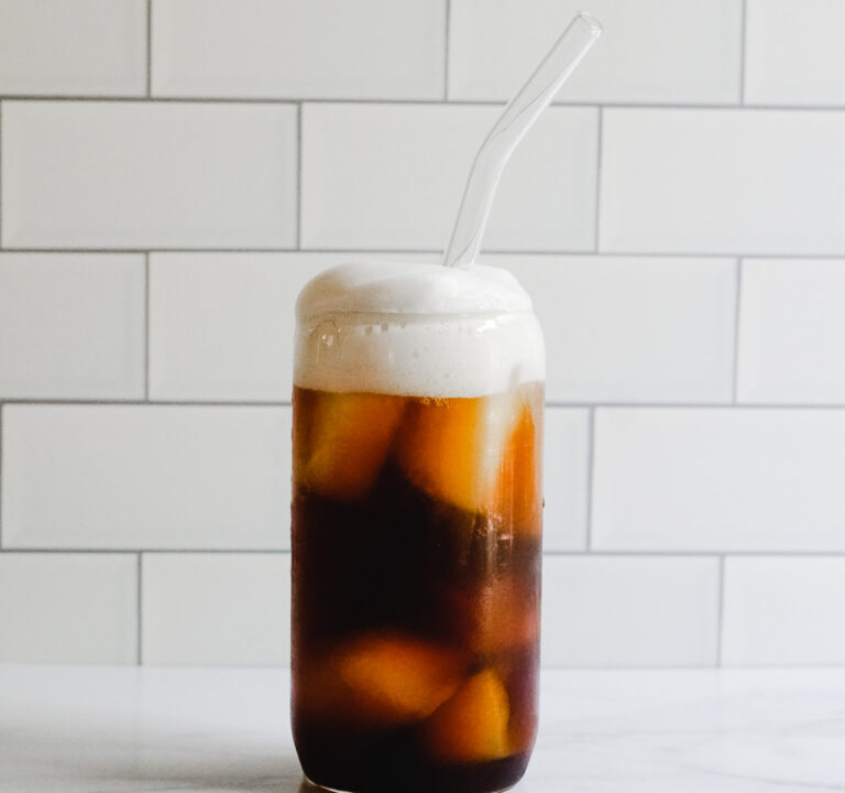 Coffee Soda in a clear glass topped with cold foam.