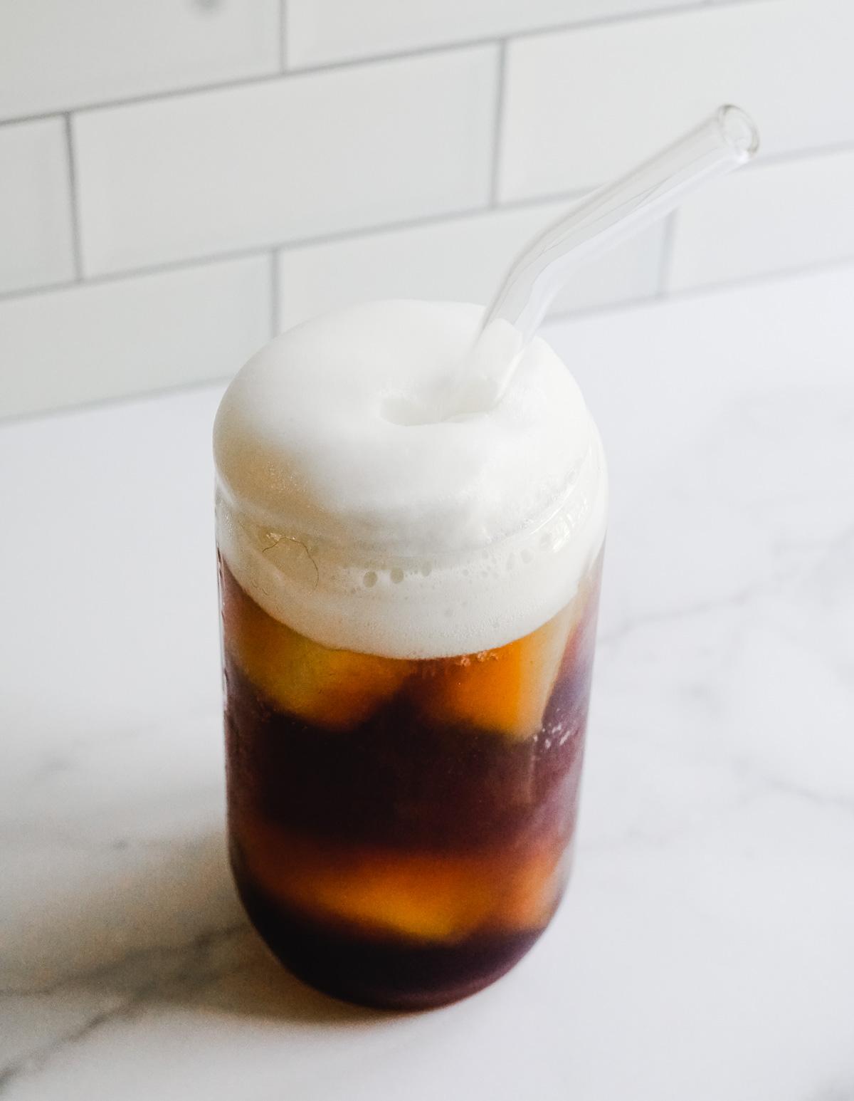 Coffee Soda in a clear glass topped with cold foam.