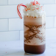Copycat Starbucks Peppermint Mocha Frappuccino Recipe in a clear glass topped with whipped cream, red sprinkles and a candy cane.