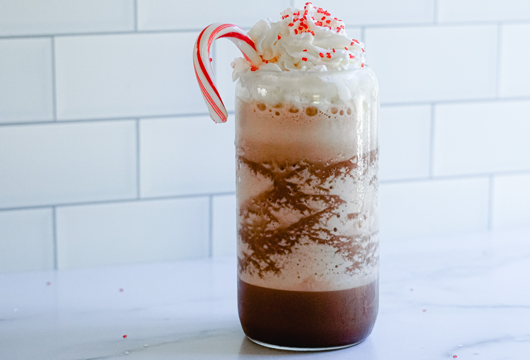 Copycat Starbucks Peppermint Mocha Frappuccino Recipe in a clear glass topped with whipped cream, red sprinkles and a candy cane.