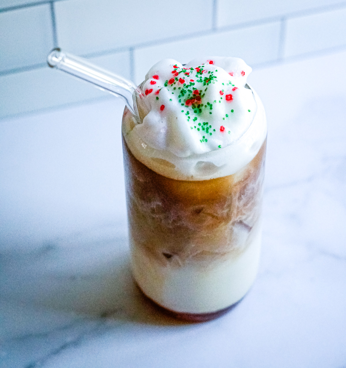 Copycat Starbucks Iced Sugar Cookie Latte in a clear glass topped with whipped cream and red and green sprinkles.