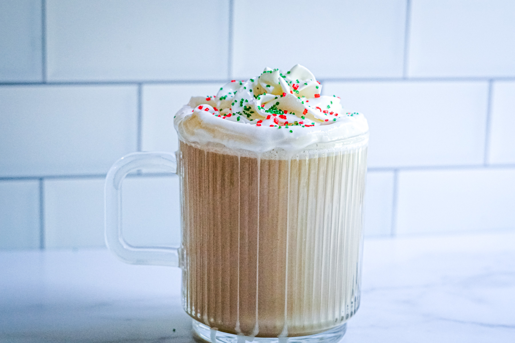 Copycat Starbucks Hot Sugar Cookie Latte in a clear mug topped with whipped cream and red and green sprinkles.