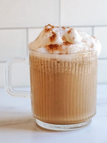 Coffee with Honey in a glass mug with frothy hot milk on top and a sprinkle of cinnamon.