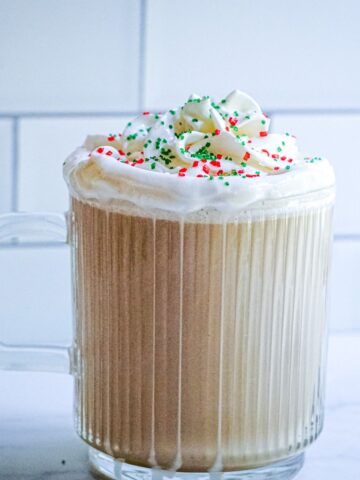 Starbucks Copycat Sugar Cookie Latte in a glass mug with whipped cream and red and green sprinkles on top.