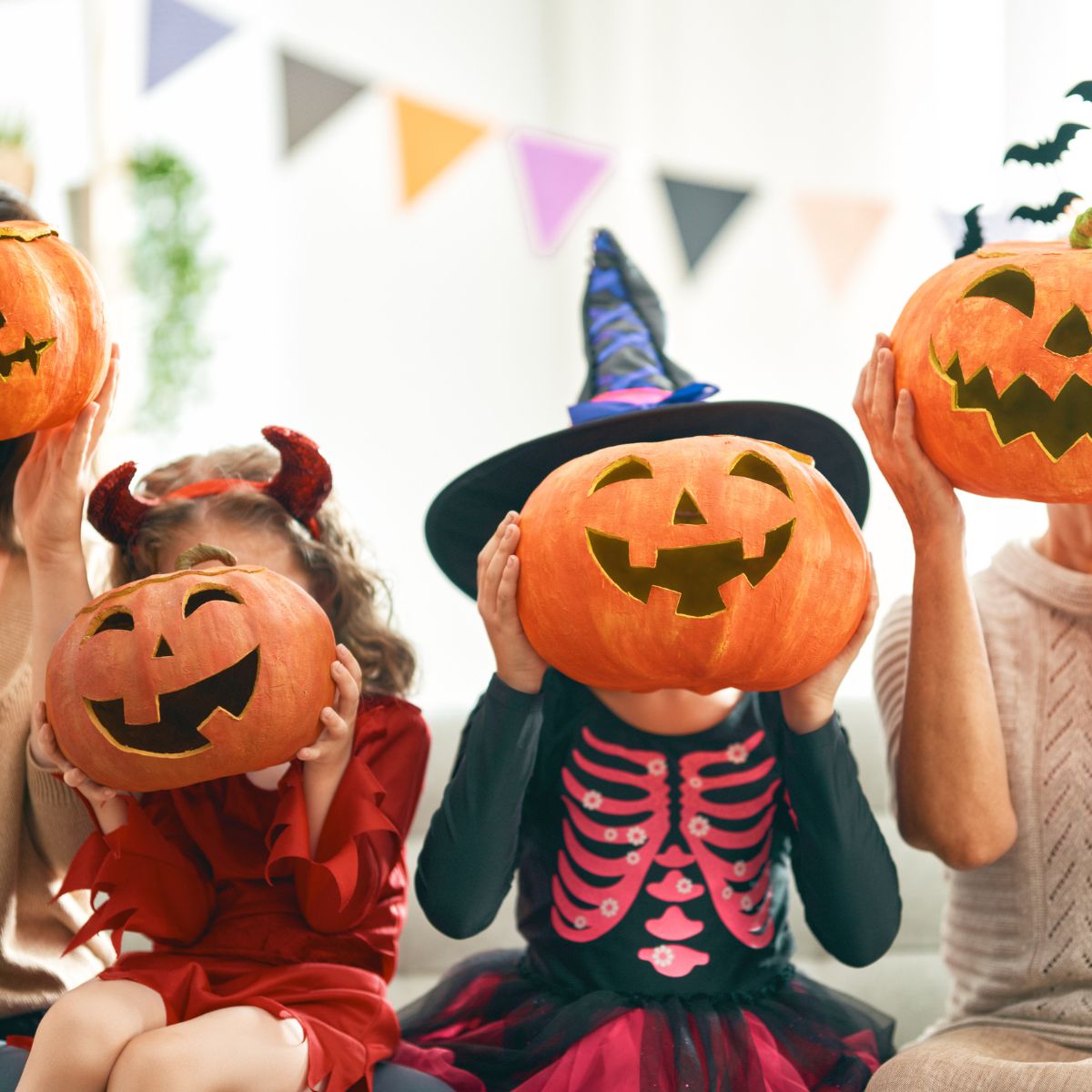 Kids in costumes at a Halloween party holding carved pumpkins in front of their faces.