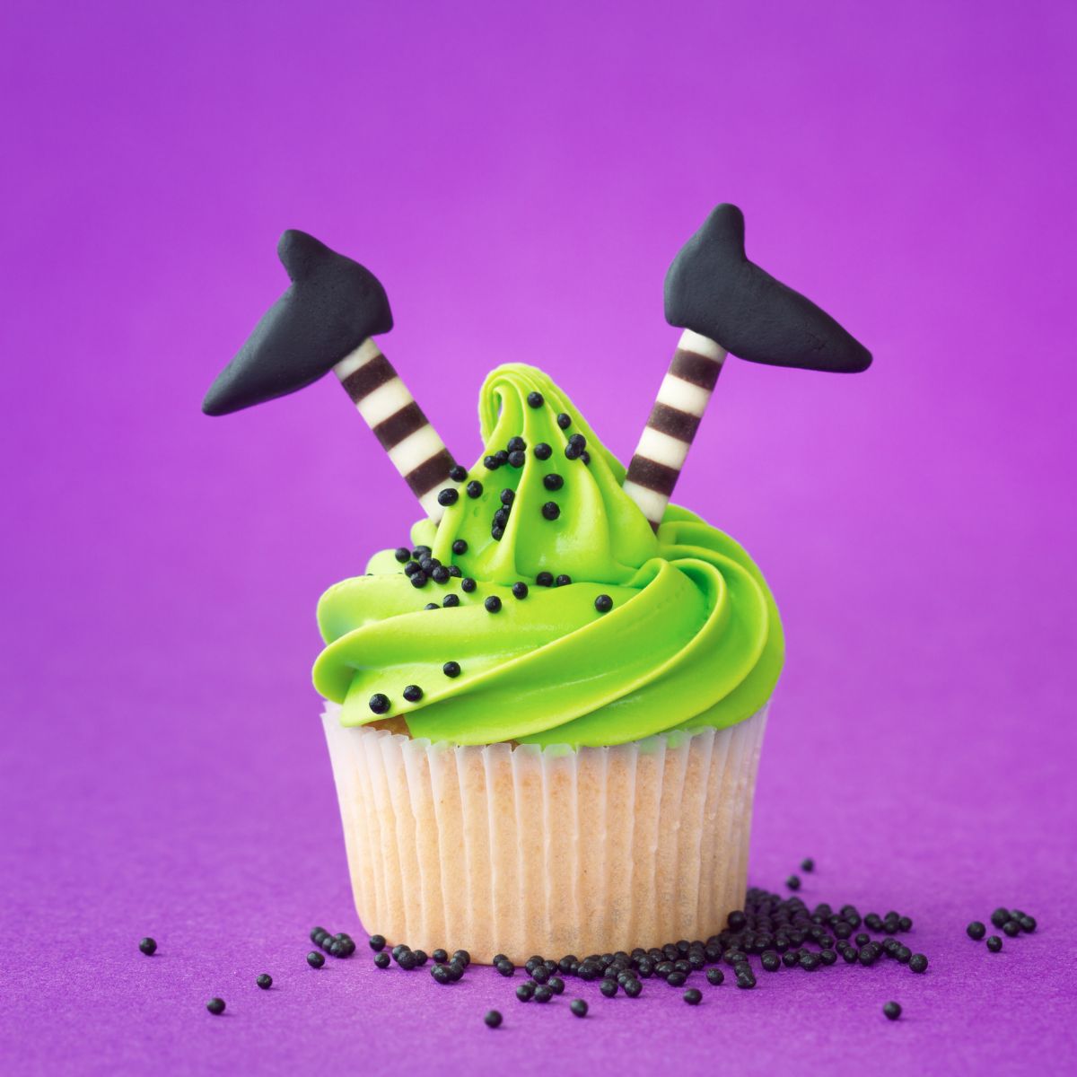 Cupcake with green frosting. Candy that looks like witches legs are sticking out of the top. Purple background.