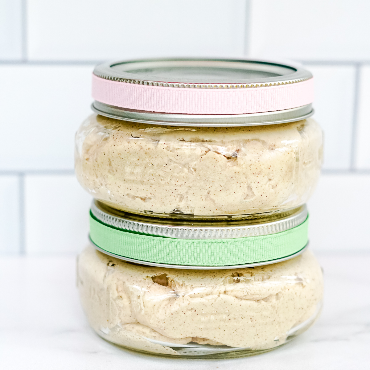 Whipped cinnamon honey butter in glass mason jars with mint green and pale pink ribbons tied around the top.