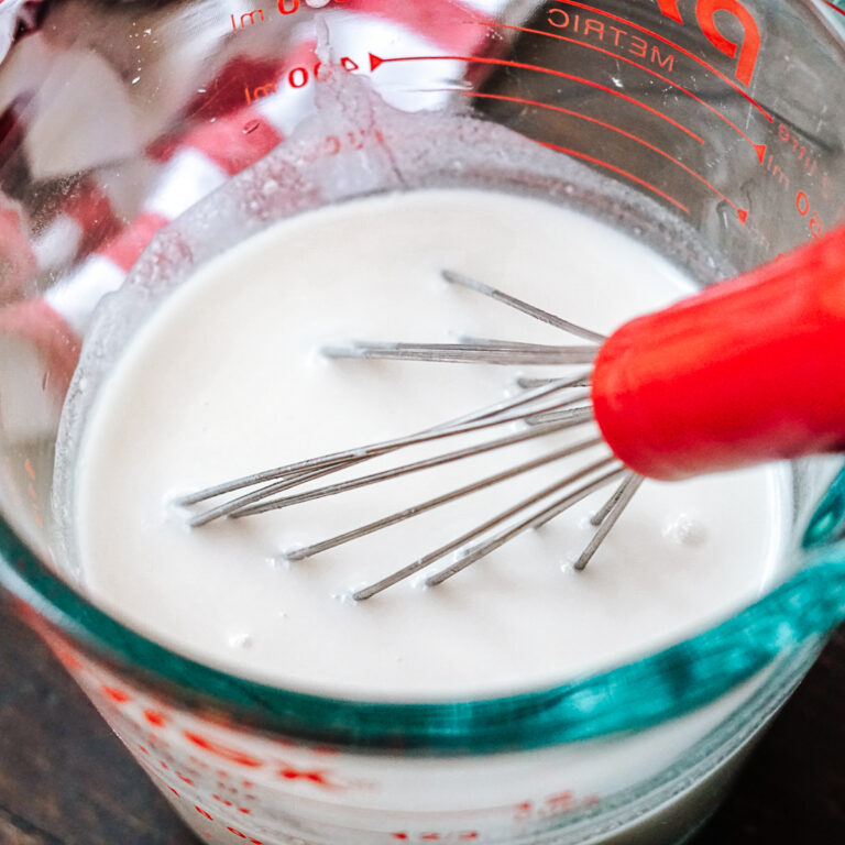 Dairy Free Buttermilk in a glass pyrex measuring cup with a red whisk