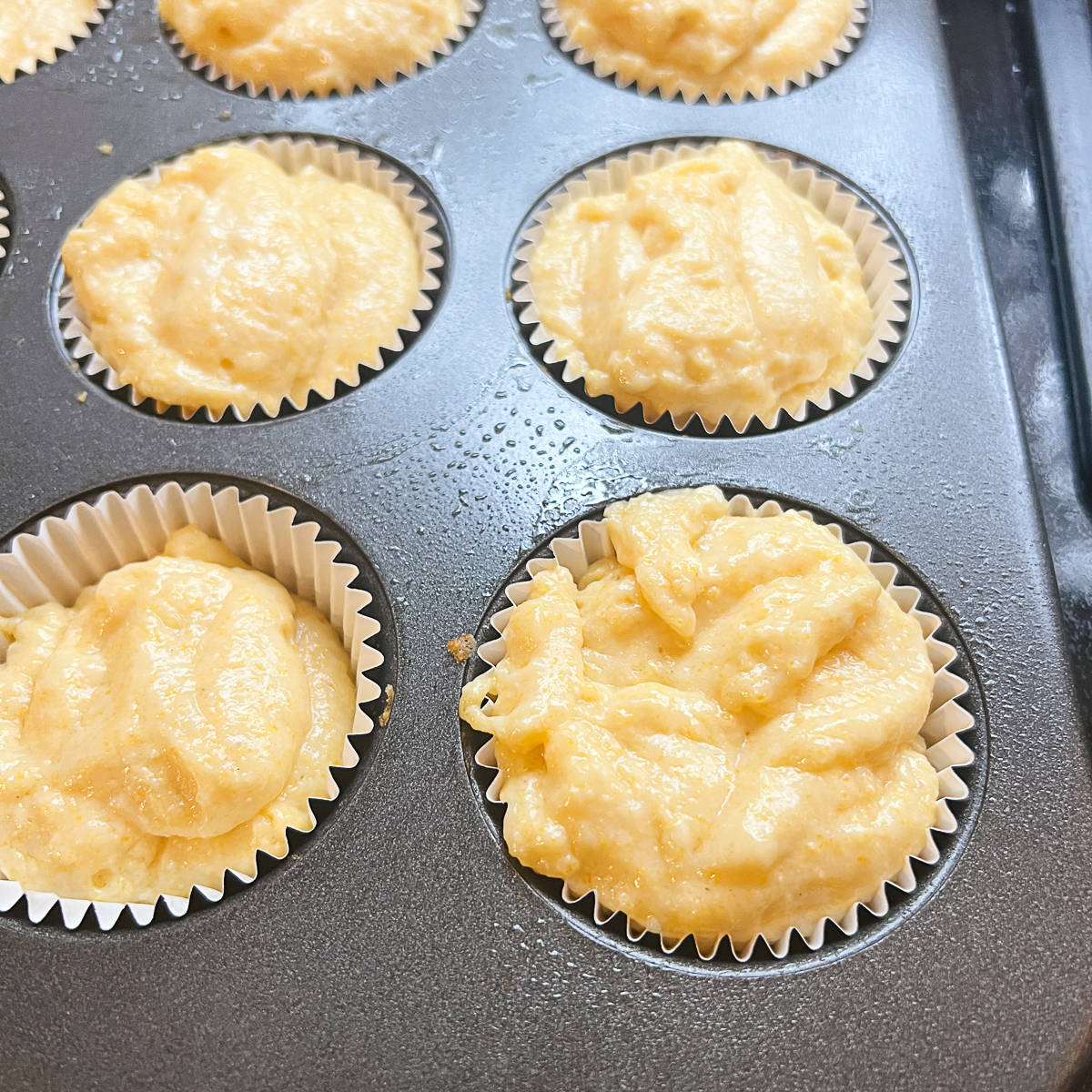 Gluten Free Cracker Barrel Cornbread Muffin batter in cupcake liners in a muffin tin ready to be baked in the preheated oven